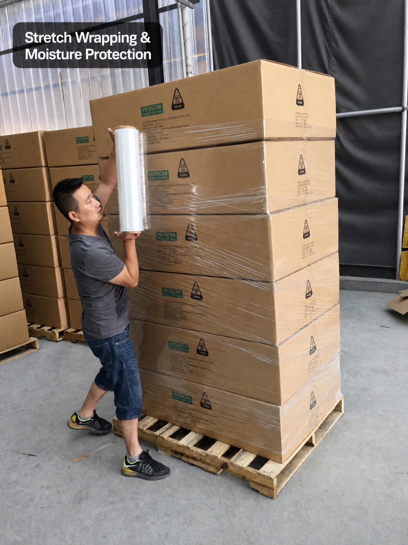 Factory worker stretch-wrapping Hitachi export cartons on a pallet